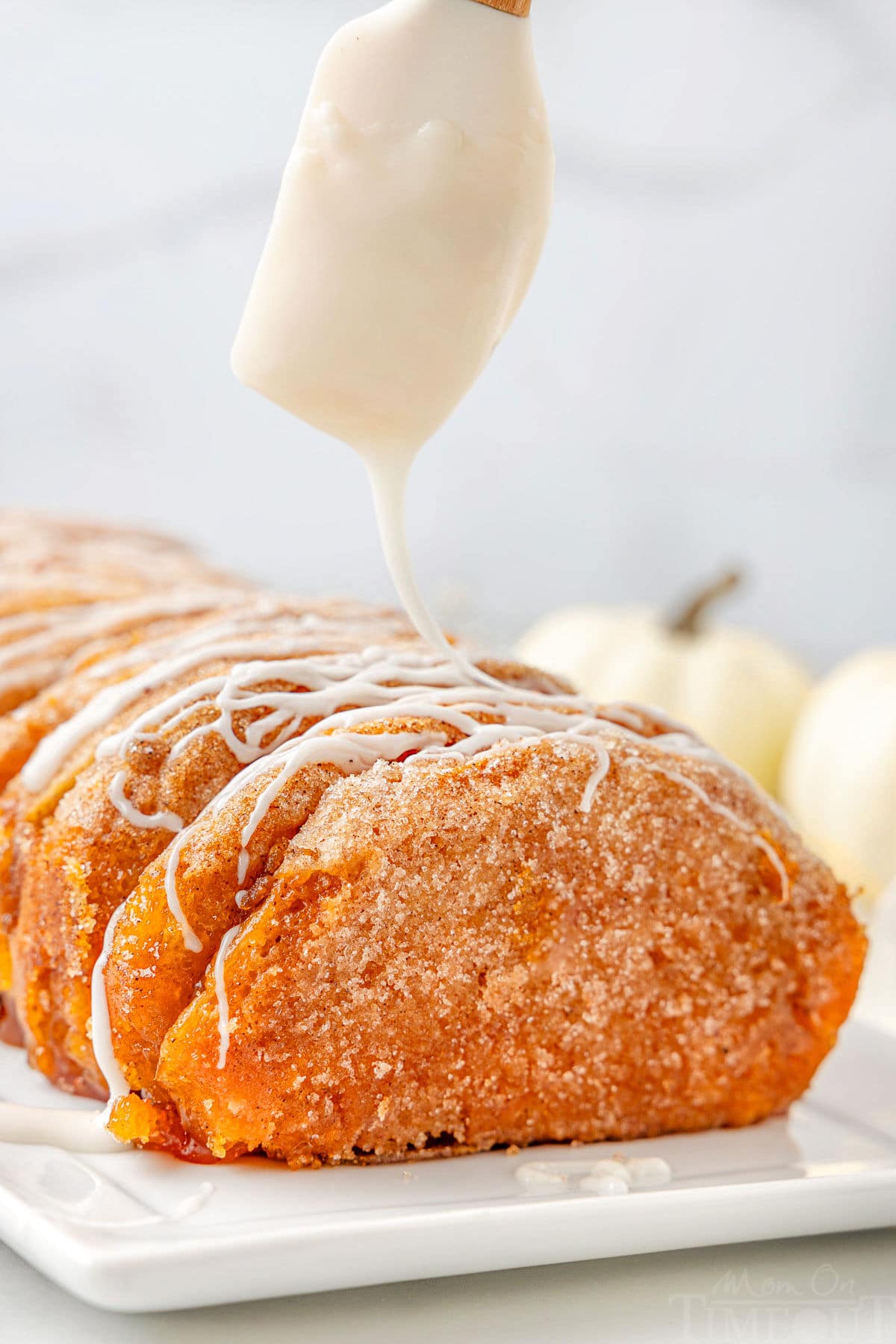 Icing being drizzle on top of a pumpkin pull apart bread made with refrigerated biscuits.