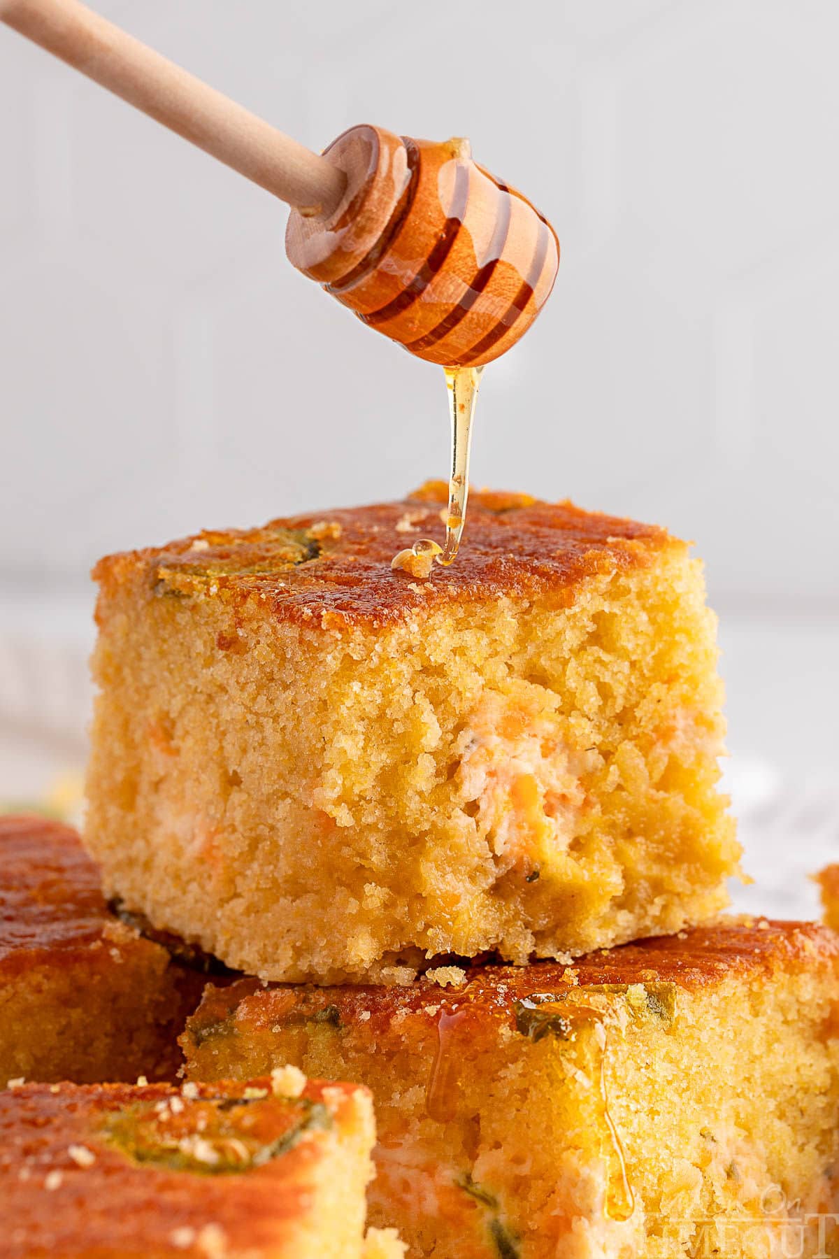 Jalapeno cornbread recipe cut into squares and stacked on each other. Honey is being drizzled over the top of the cornbread.