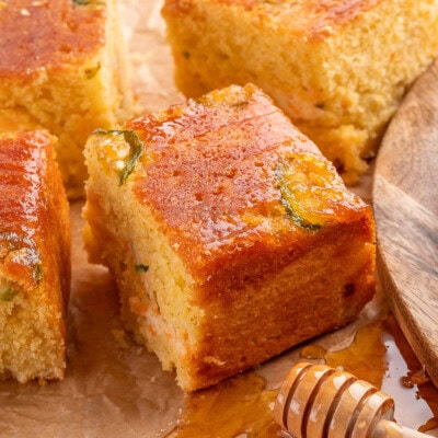 Jalapeno Cornbread recipe cut into squares on parchment paper with honey dripping onto the paper.