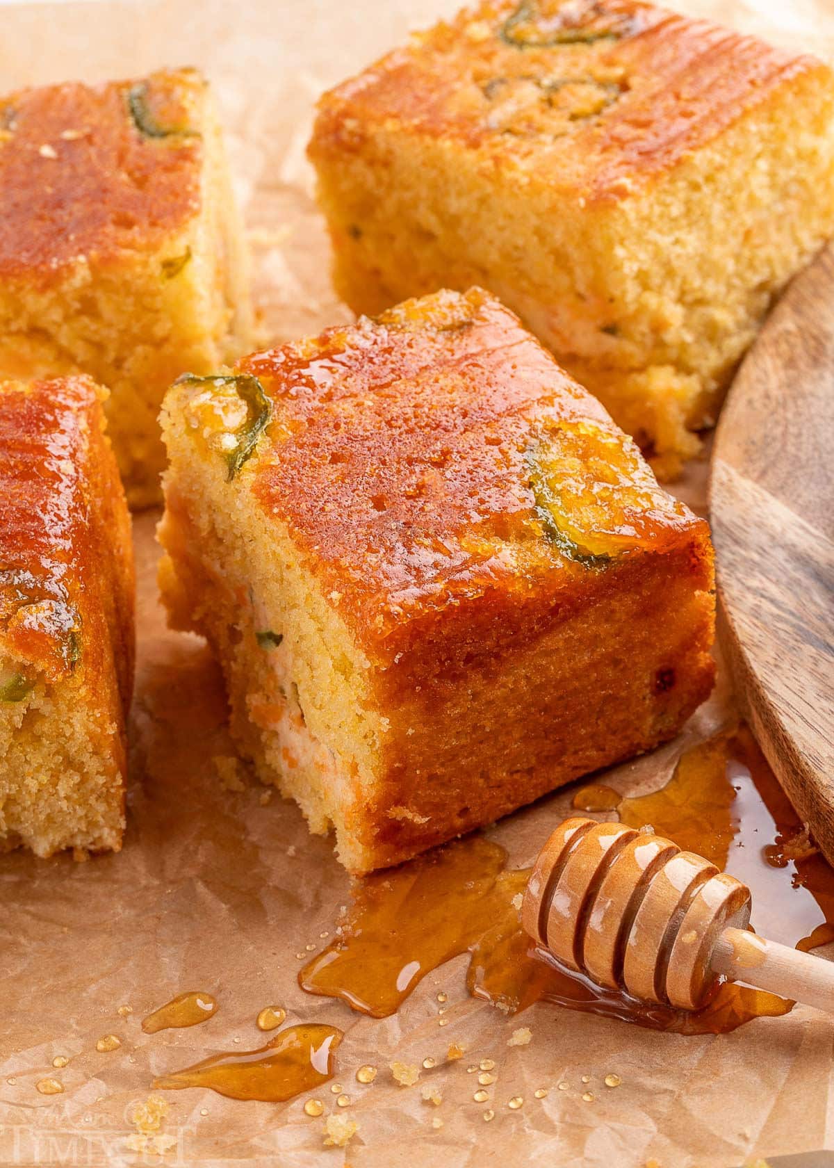 Jalapeno Cornbread recipe cut into squares on parchment paper with honey dripping onto the paper.