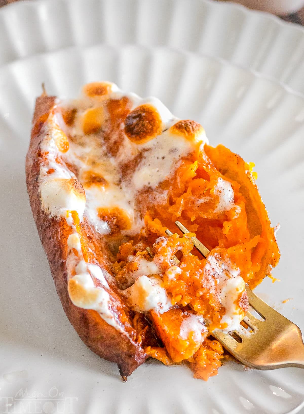 A twice baked sweet potato on a white plate with a gold fork in the potato.