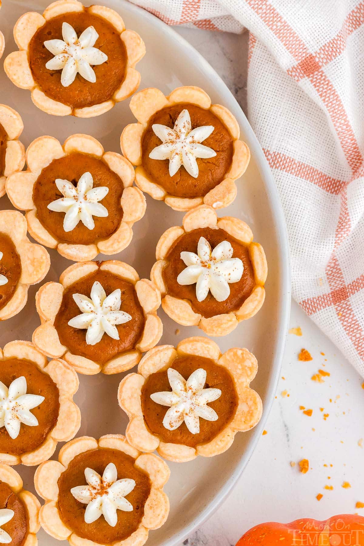 Top down shot of mini pumpkin pies with whipped cream dollops on a plate with an orange and white linen napkin off to the side.