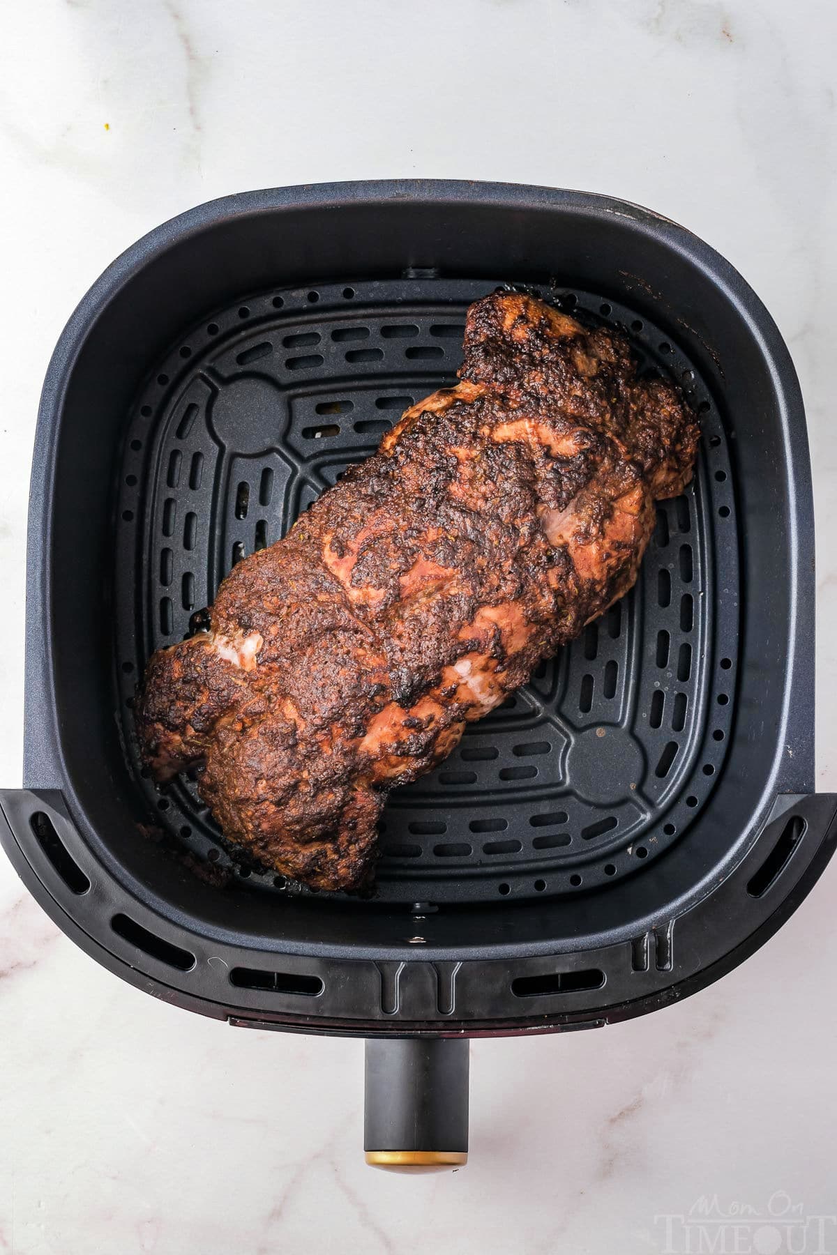 Top down view of pork tenderloin in air fryer sitting on white surface.