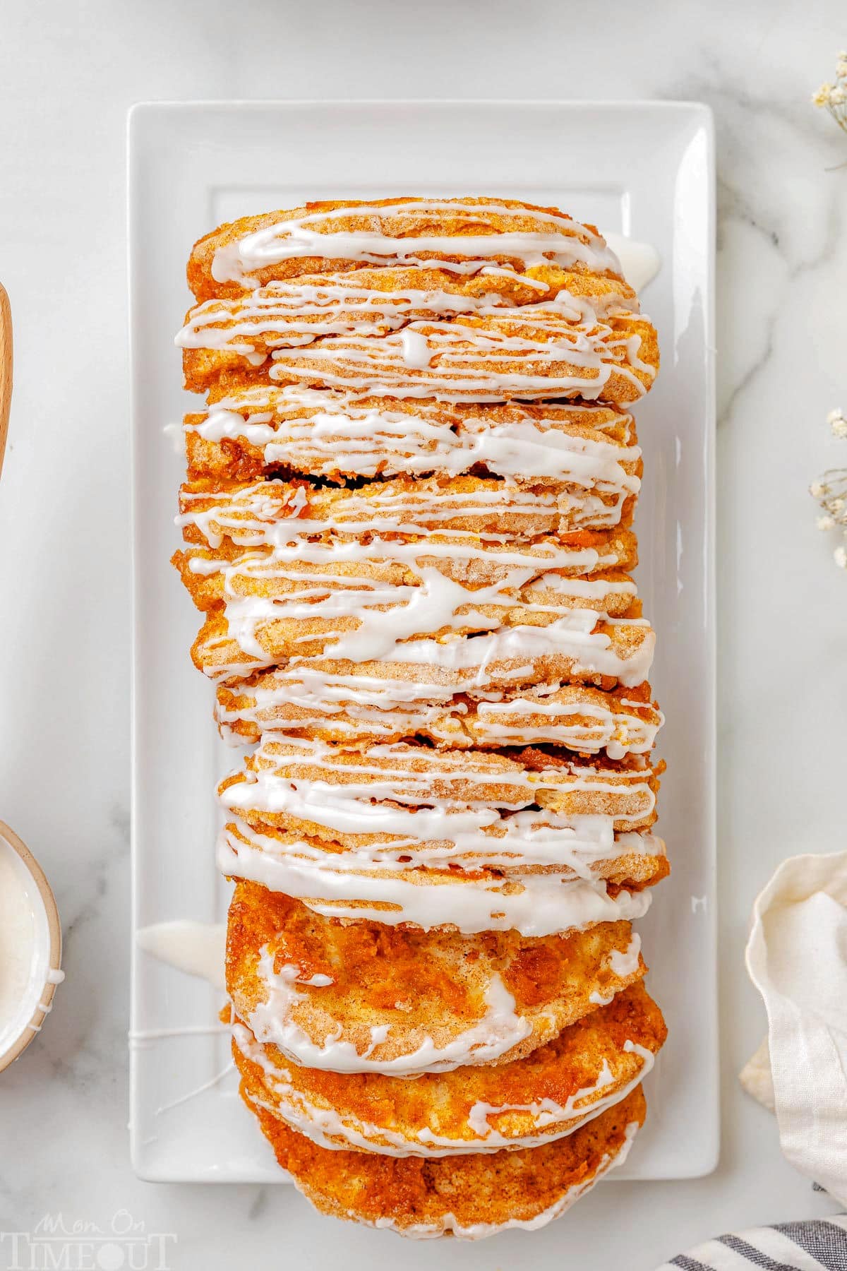 Top down view of pumpkin pull apart bread recipe topped with a simple vanilla glaze on a white rectangular plate. Two slice have been pulled away from the loaf.