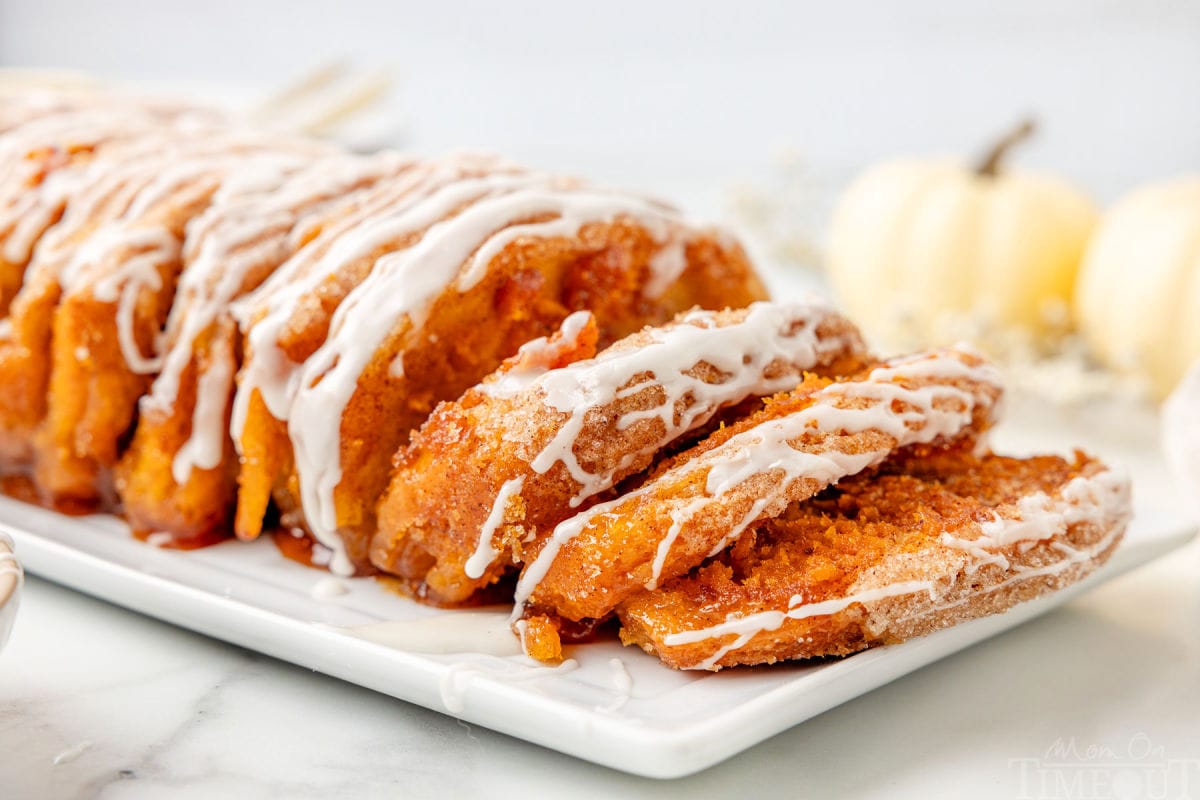 Side profile shot of pull apart pumpkin bread on a white plate topped with a glaze. Pieces have been pulled down to show the pumpkin filling.