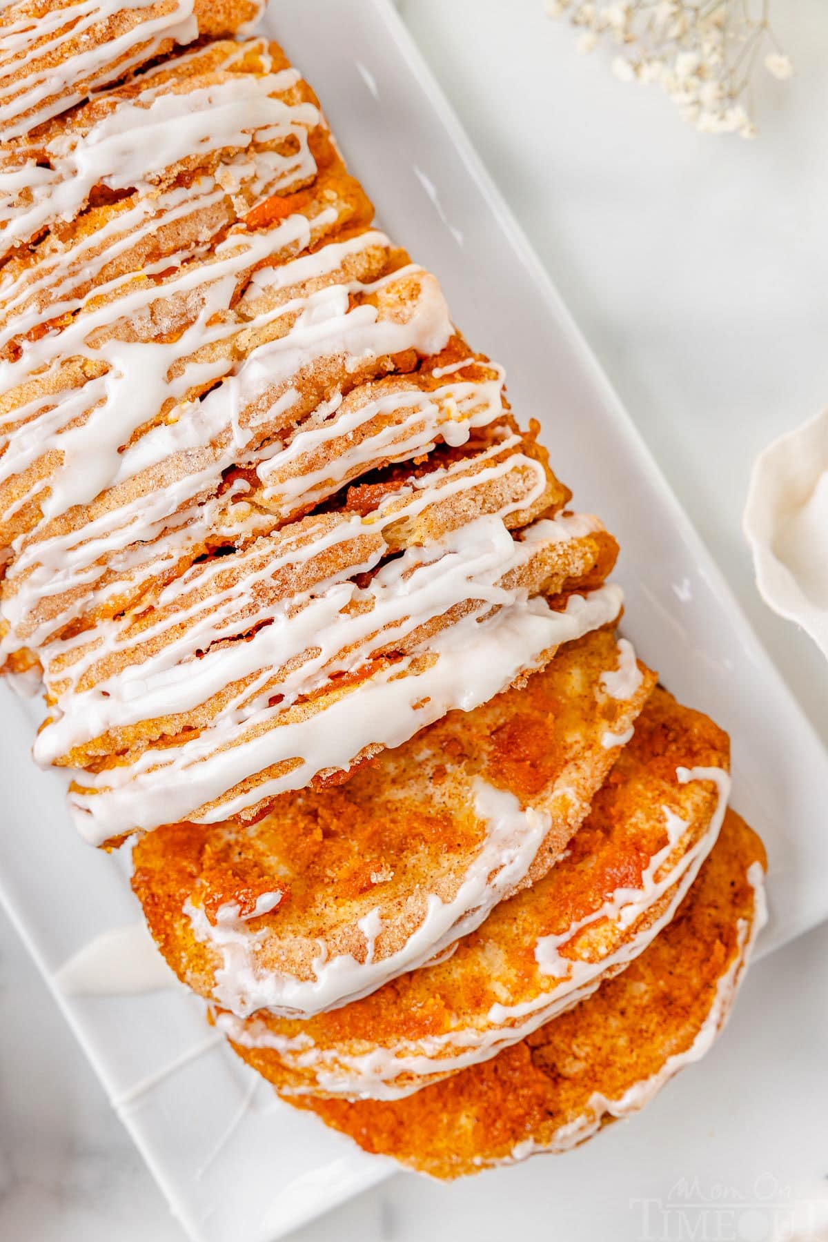 Top down view of pumpkin pull apart bread recipe topped with a simple vanilla glaze on a white rectangular plate. Two slice have been pulled away from the loaf.