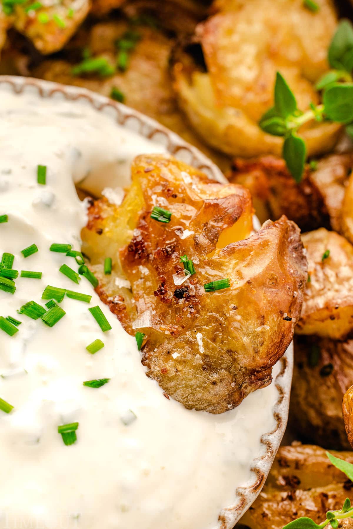 Smashed potato being dipped into a sour cream based herb dip.