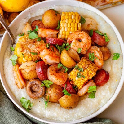 Shrimp boil in a bowl served with grits. The bowl is sitting next to a sheet pan with the rest of the shrimp boil.