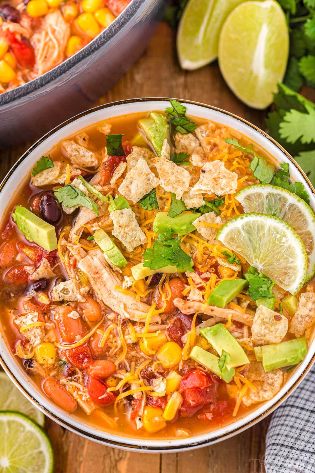 A top down shot of chicken taco soup in a bowl with lime slices next to the bowl.