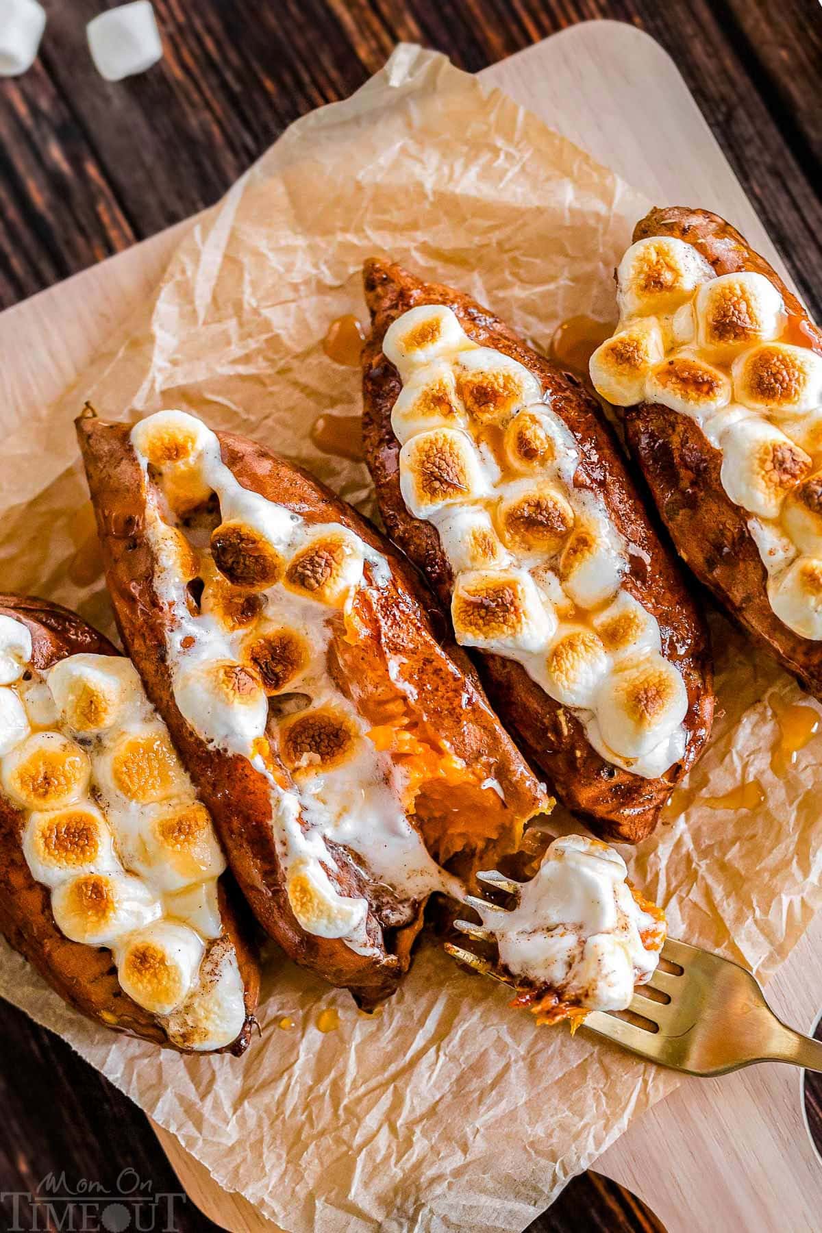 Twice baked sweet potatoes on a piece of parchment paper with a gold fork digging into a potato.