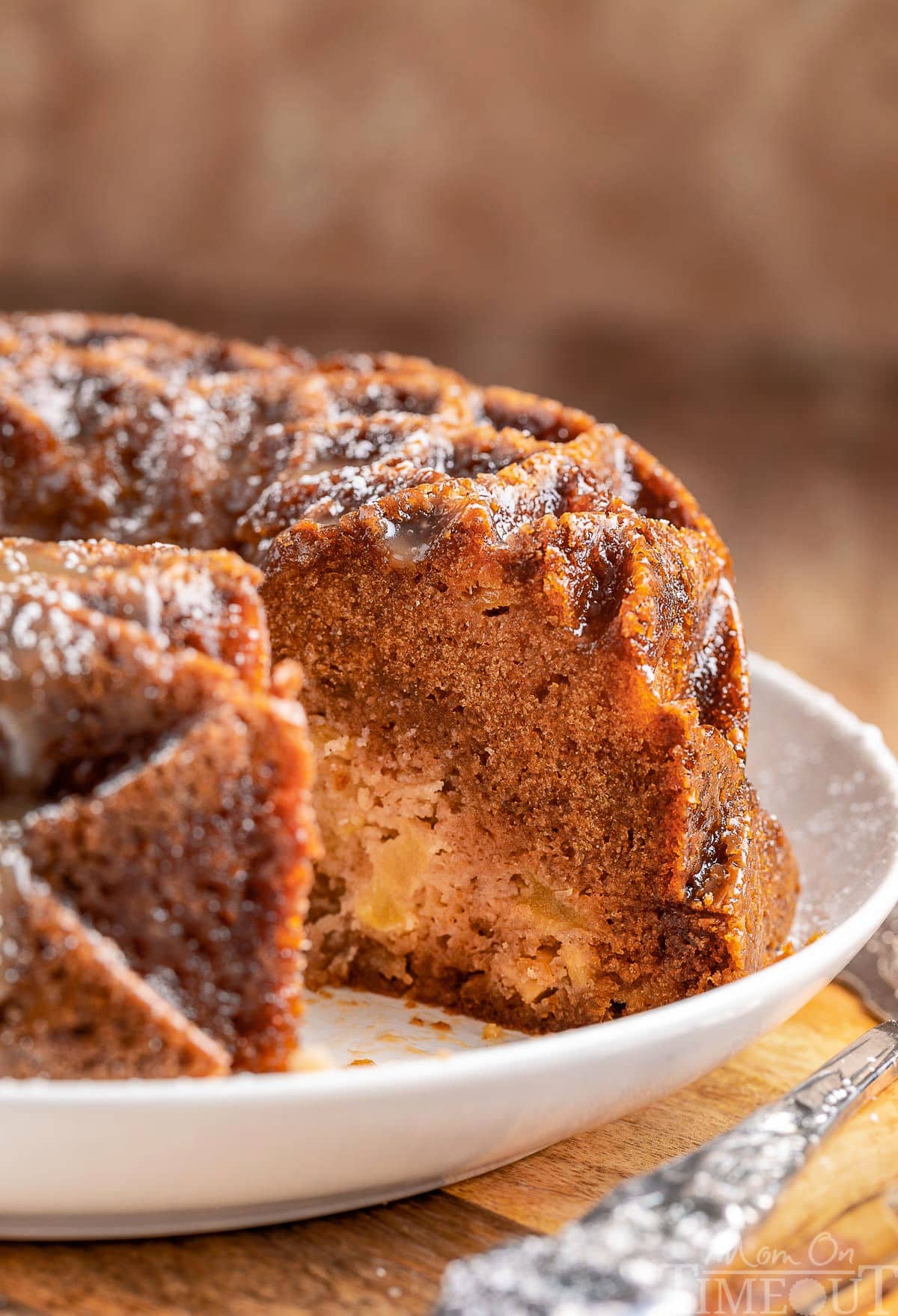 Apple bundt cake with one piece removed so you can see the profile of the cake. The cake is on a white serving dish.