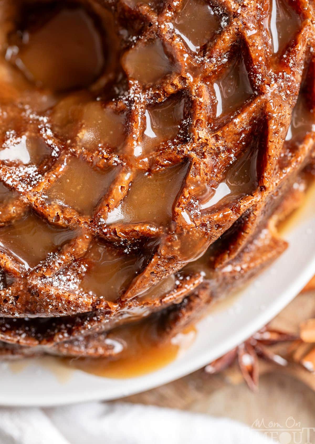 Top down view of caramel apple bundt cake on white cake plate. Shiny caramel pools in all the nooks and crannies of the bundt cake.