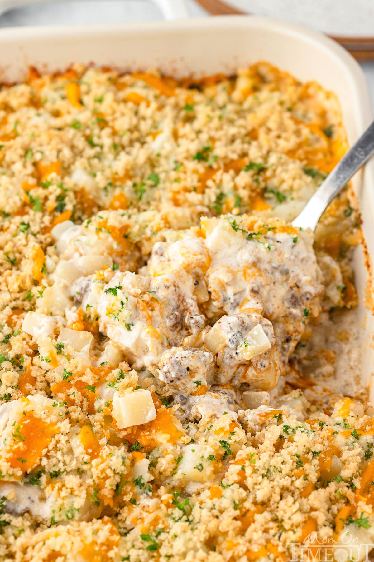 Casseroles with ground beef in serving dish with large serving spoon scooping out the casserole.