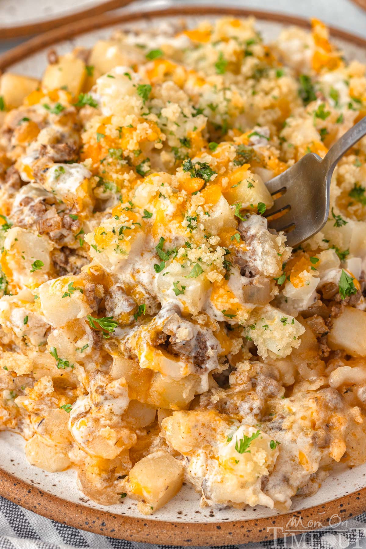 Cose up of ground beef and potato casserole recipe plated with a fork digging into the cheesy casserole.