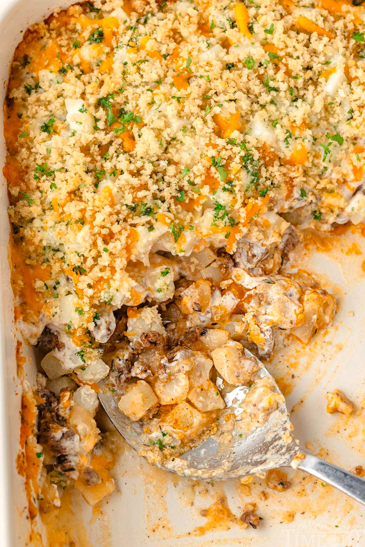 Top down look at ground beef casserole recipe in casserole dish with about half removed. A large serving spoon is resting in the dish.