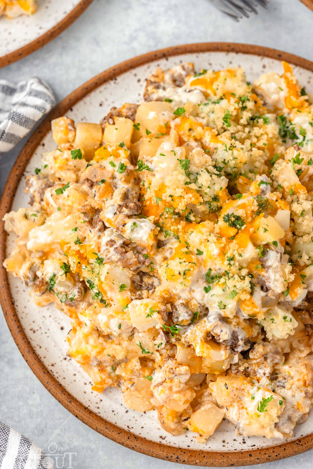 Top down look at ground beef and potato casserole plated on a round inner plate and topped with chopped parsley.