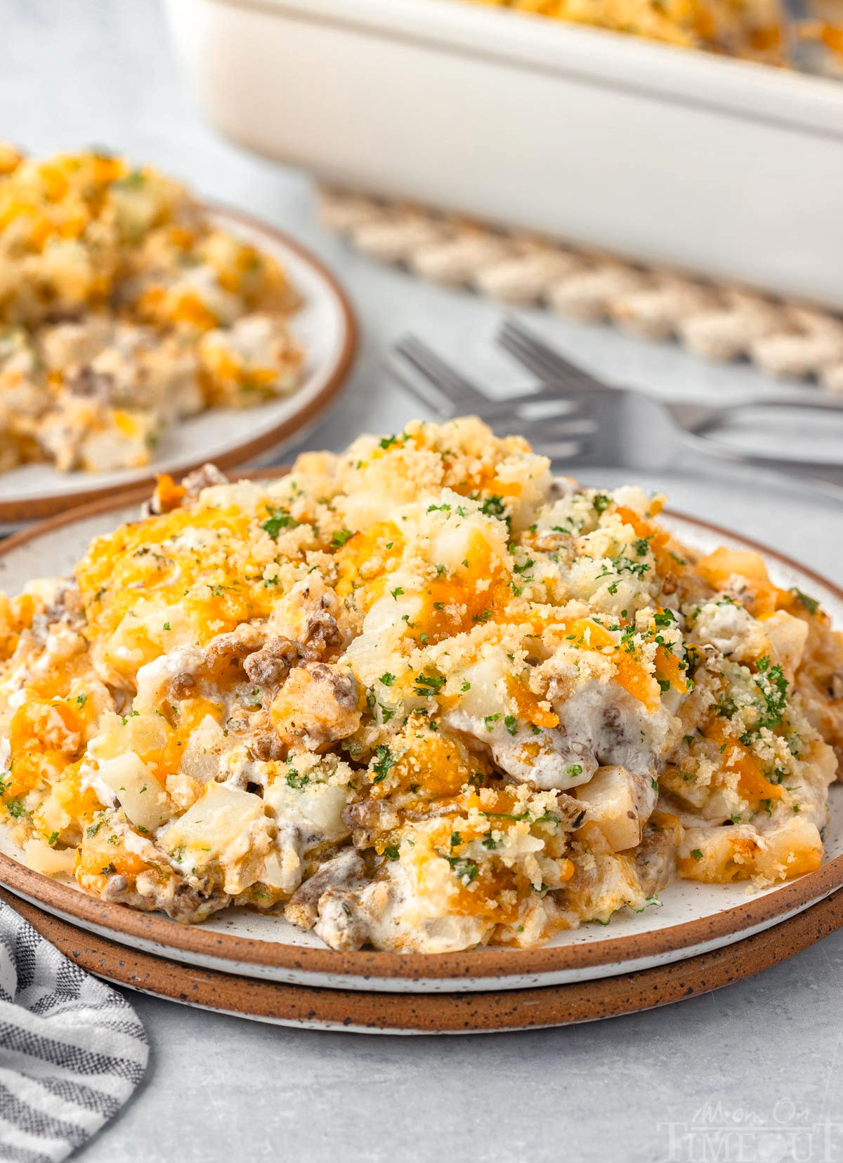 Front view of ground beef potato casserole on a plate with a brown rim and casserole dish in background.