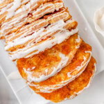 Top down view of pumpkin pull apart bread recipe topped with a simple vanilla glaze on a white rectangular plate. Two slice have been pulled away from the loaf.