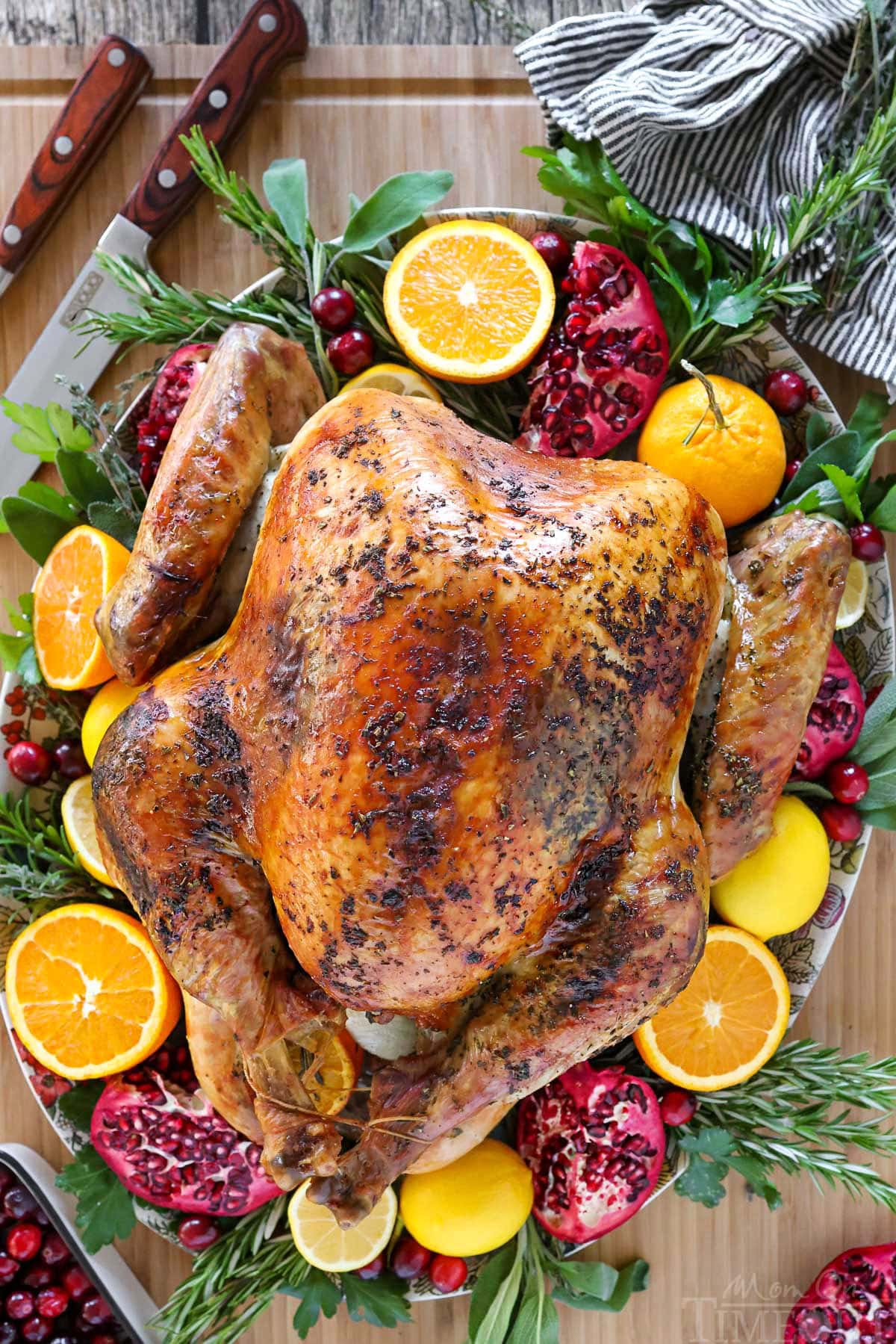 Top down view of the best thanksgiving turkey recipe on a serving platter with oranges, lemons, pomegranates, fresh herbs and cranberries.