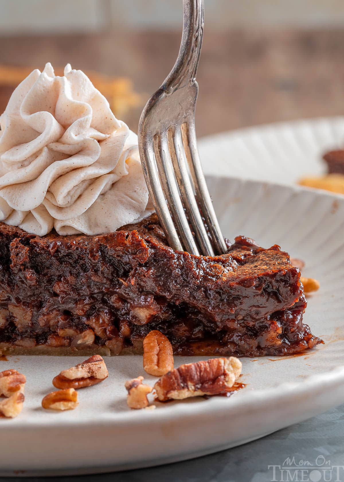 Fork cutting into the end of a slice of bourbon chocolate pecan pie on a white plate.