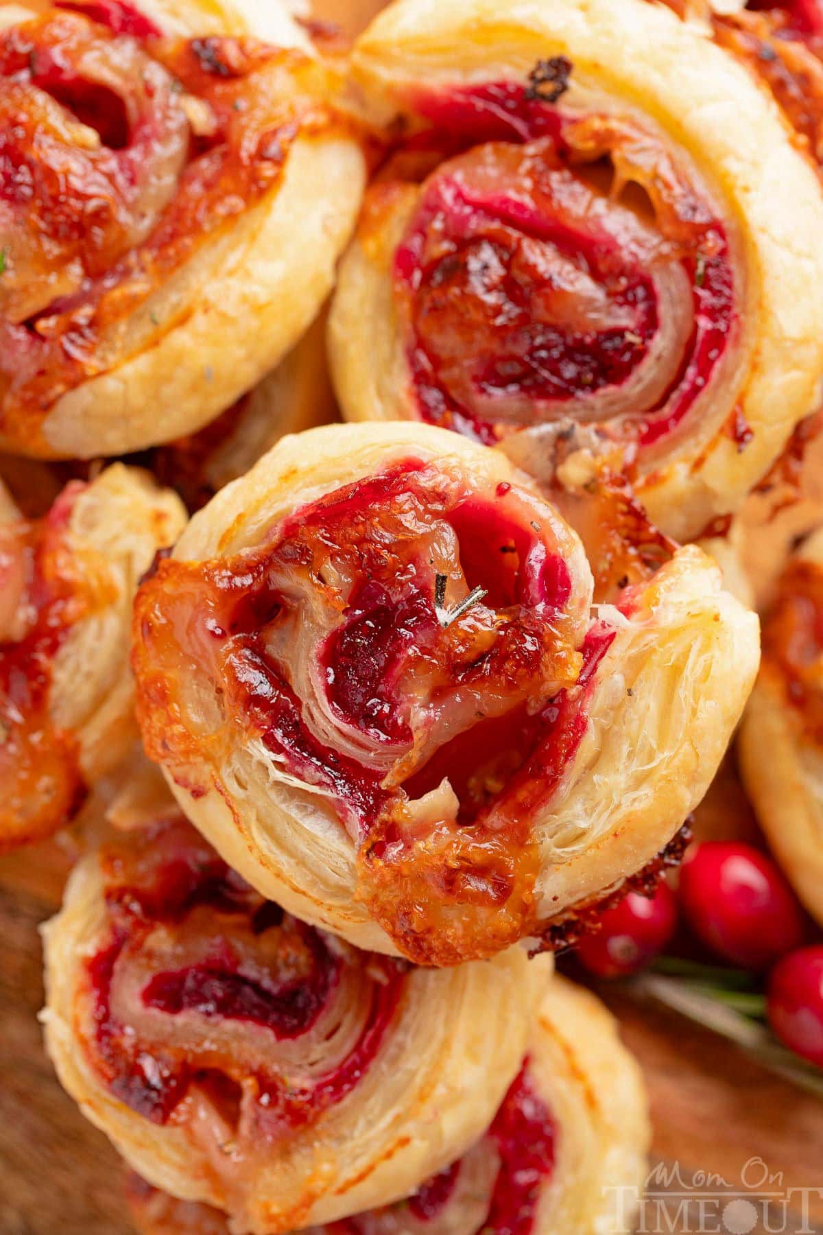 Top down shot of brie and cranberry puff pastry pinwheels stacked on a wood board.