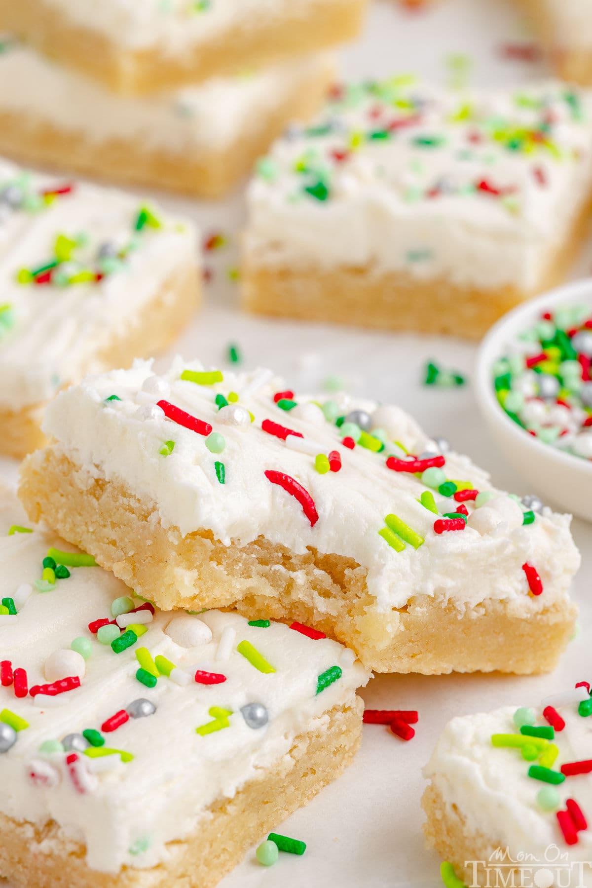 A sugar cookie bar with a bite taken out of it. The bar is resting on another bar with more bars in the background.