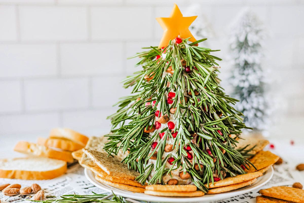 Christmas Tree Cheese Ball on a white plate with crackers surround it. Cheese ball is topped with a cheddar cheese star.