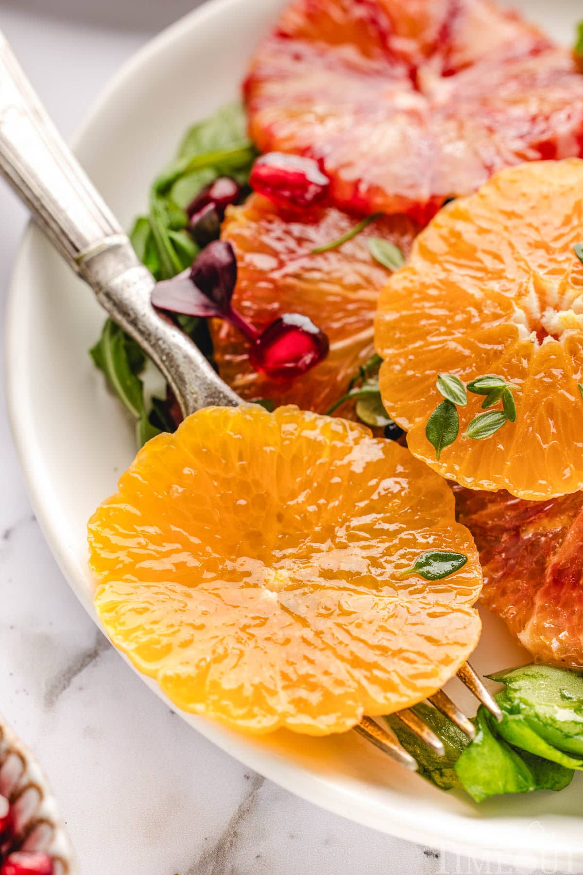 Close up of orange slices, arugula, pomegranate seeds all tossed with citrus salad dressing.