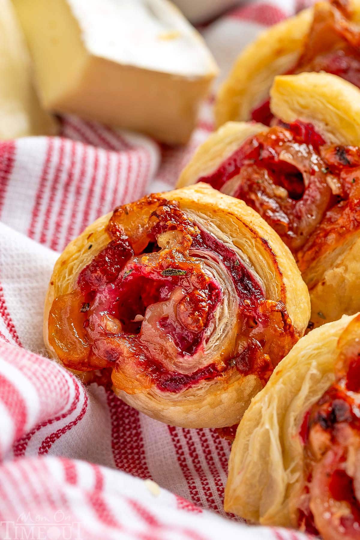 Cranberry brie appetizers made with puff pastry in a basket lined with a red and white striped towel.