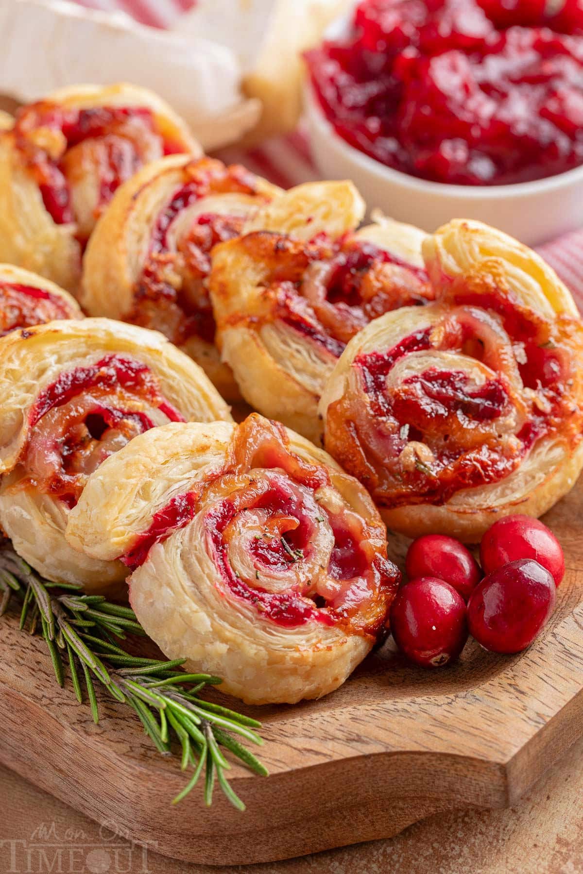 Wood serving tray filled with cranberry brie pinwheels, fresh rosemary and cranberries.