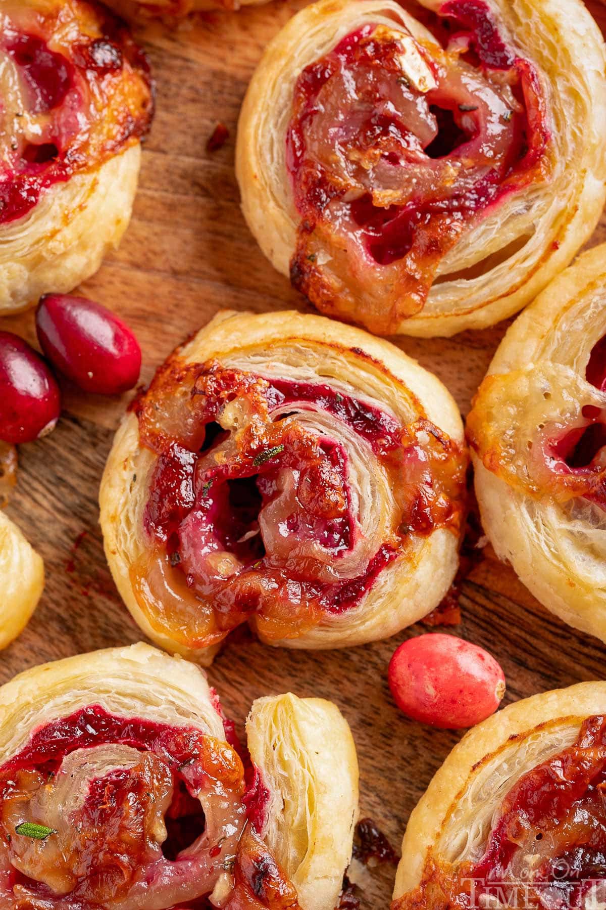 Top down shot of brie and cranberry puff pastry pinwheels on a wood board with fresh cranberries scattered about.