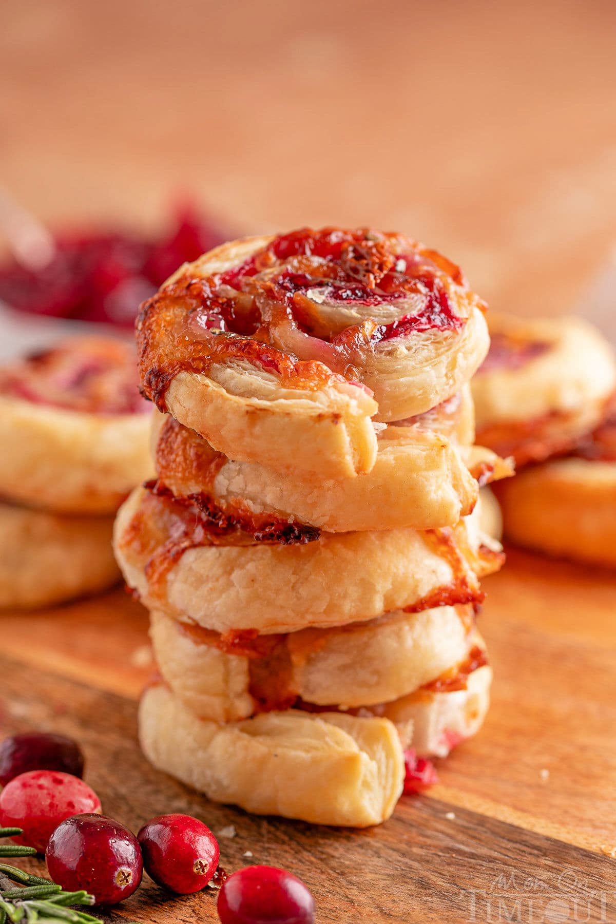 Five cranberry brie puff pastry appetizers stacked on each other on a wood board with fresh cranberries scattered about.