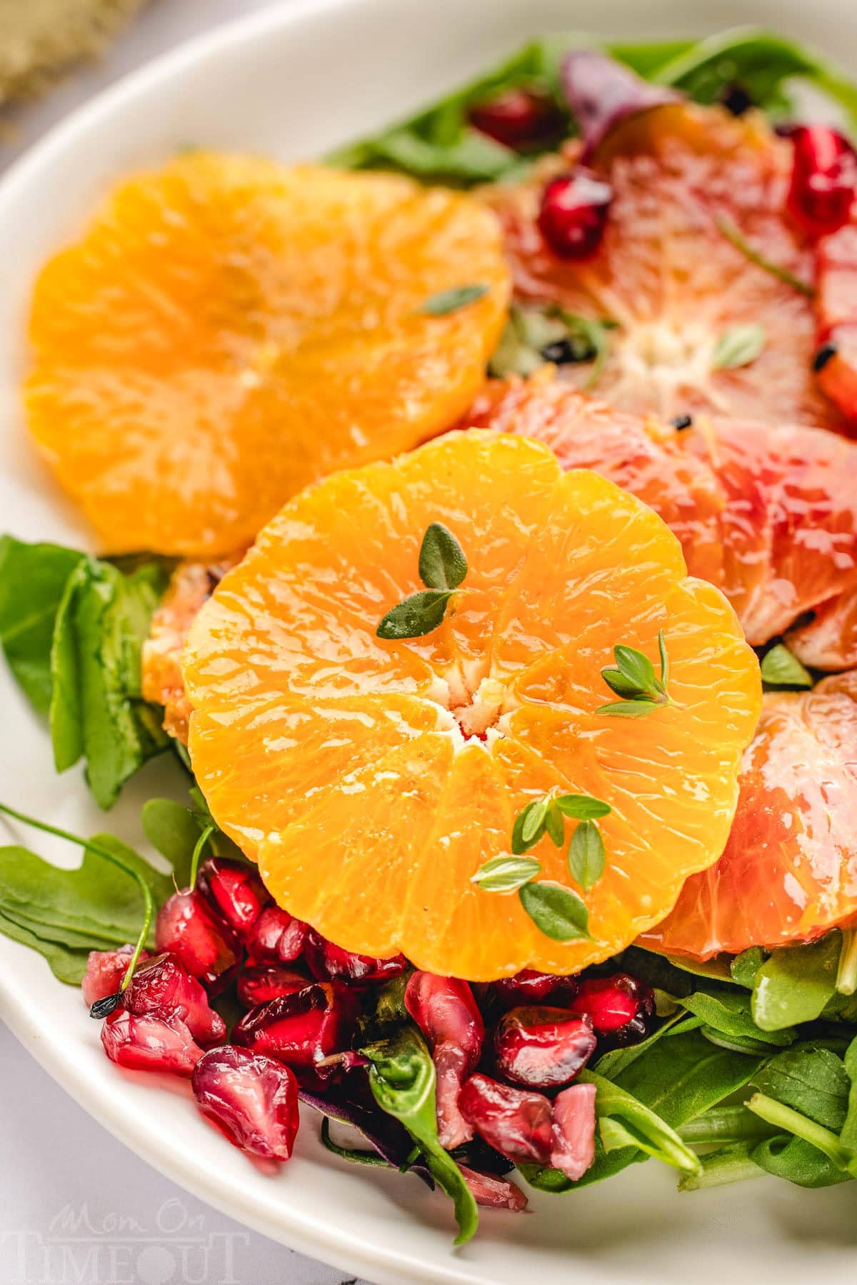 Close up of orange slices, arugula, pomegranate seeds all tossed with dressing for citrus salad.