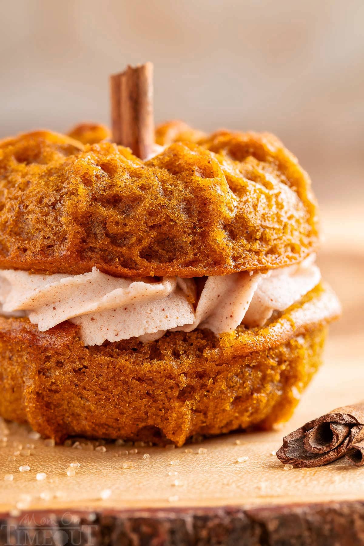 Close up front partial view of a mini pumpkin bundt cake with brown butter cinnamon frosting sitting on a wood board. A cinnamon stick can be seen sticking out of the top of the cake for the "stem".