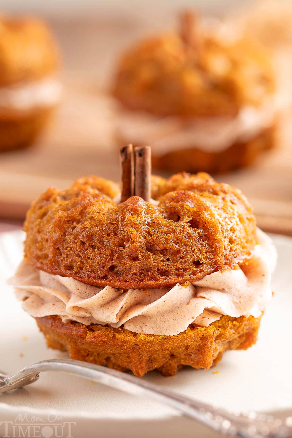 Mini pumpkin bundt cake made with two small bundts and sandwiched with cinnamon brown butter frosting. The stem is a cinnamon stick. The cake is sitting on a white plate with a fork.