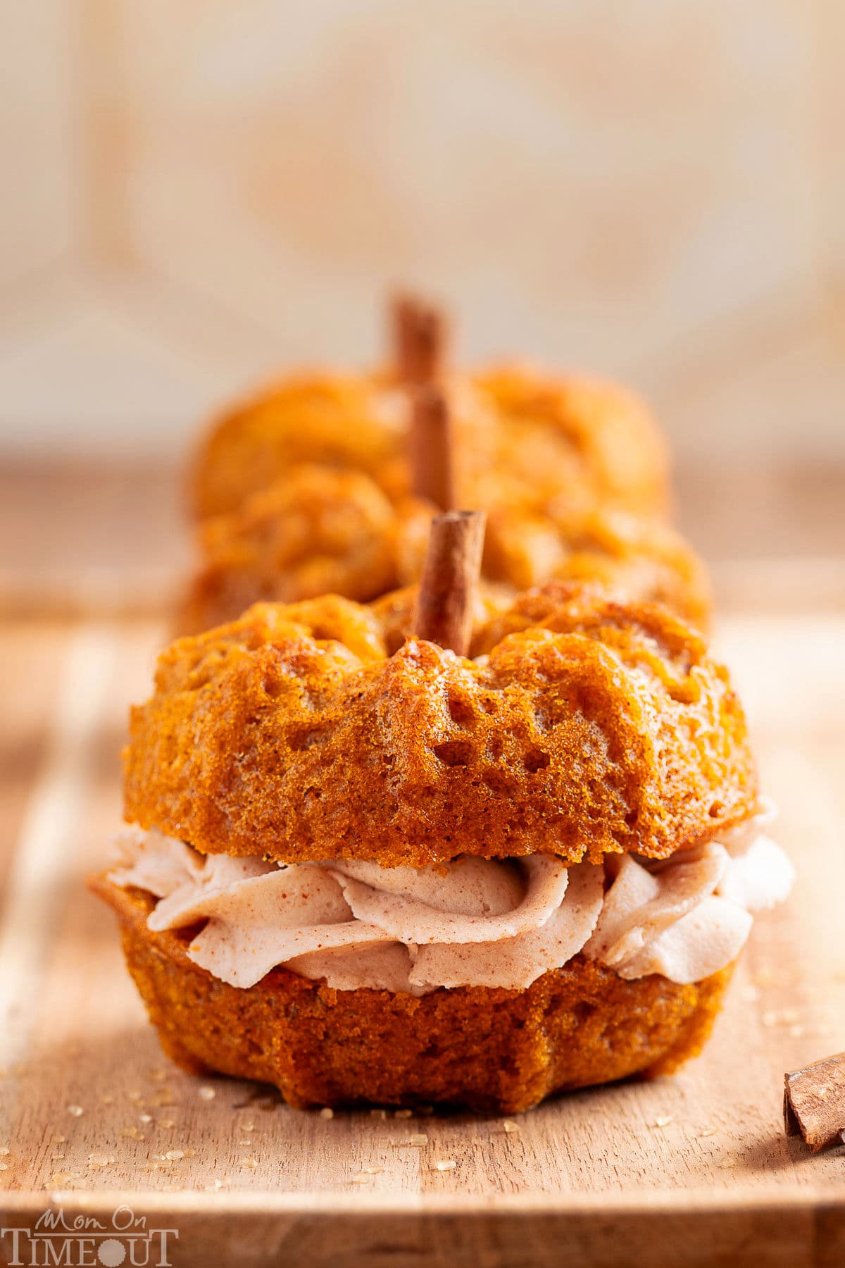 Three mini pumpkin bundt cakes lined up in a row on a wood board. Each cake is sandwiched together with brown butter frosting.