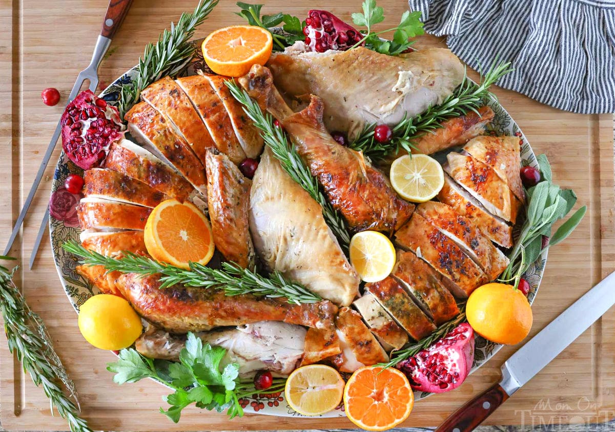 Top down view of Thanksgiving Turkey recipe plated on a large platter with fruit and herbs. Platter is sitting on a large cutting board.