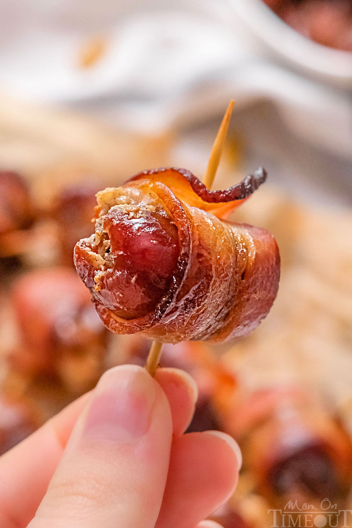 Bacon wrapped date being held up with a toothpick through the date.