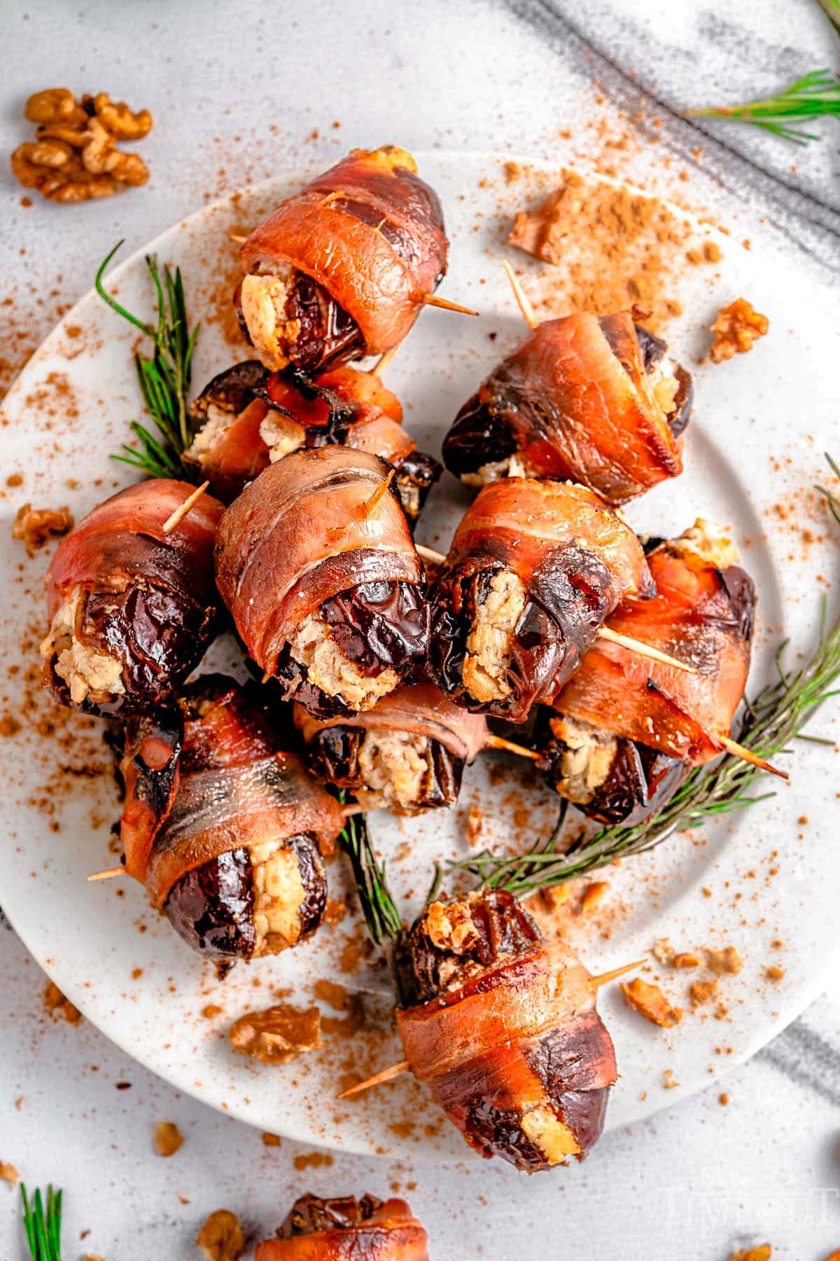 Top down view of plate of bacon wrapped dates garnished with rosemary.