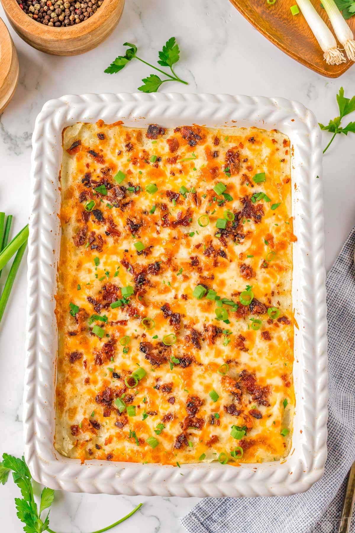 Top down look at baked mashed potatoes in white casserole dish topped with cheese and bacon.