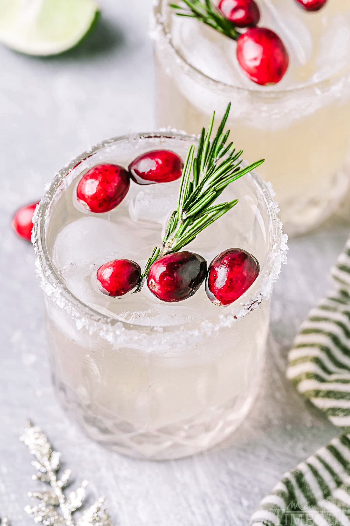 Angled down look at Christmas margaritas in short glasses with a sugared rim. The margaritas are garnished with fresh cranberries and rosemary.