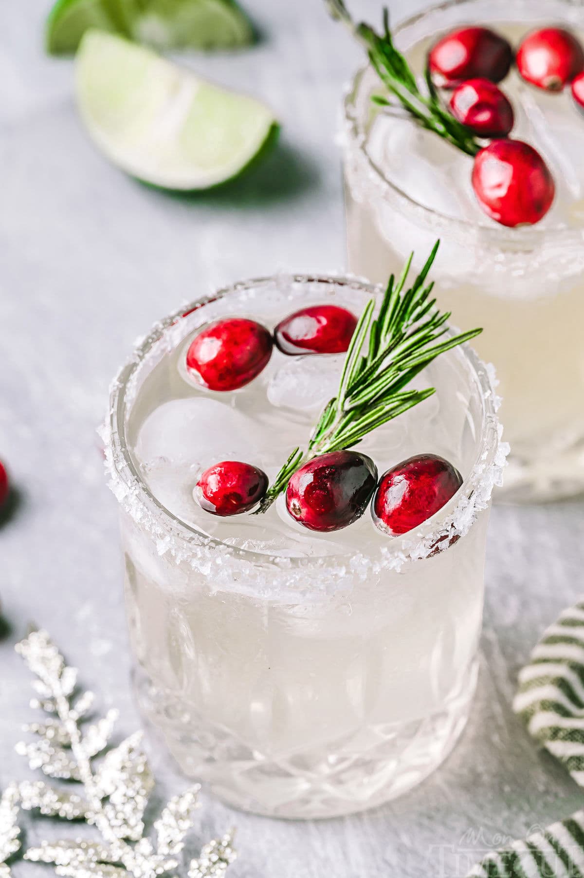 Angled down look at Christmas margaritas in short glasses with a sugared rim. The margaritas are garnished with fresh cranberries and rosemary.