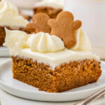 A slice of gingerbread cake topped with gingerbread men. The cake is on a white plate.