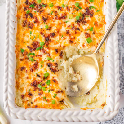 Top down look at mashed potato casserole in a white baking dish with a gold serving spoon resting in the dish where a serving has been removed.