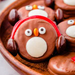 OREO Penguin propped up on a wood tray next to more penguin cookies. Penguin has red earmuffs.