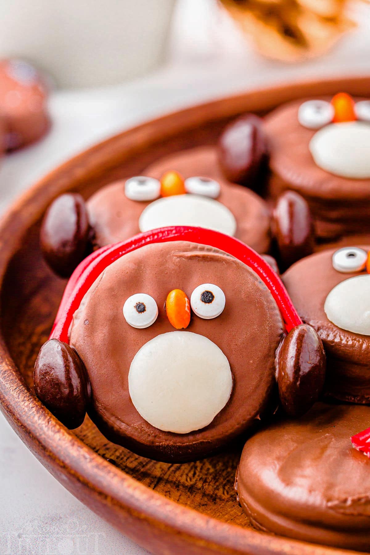 OREO Penguin propped up on a wood tray next to more penguin cookies. Penguin has red earmuffs.