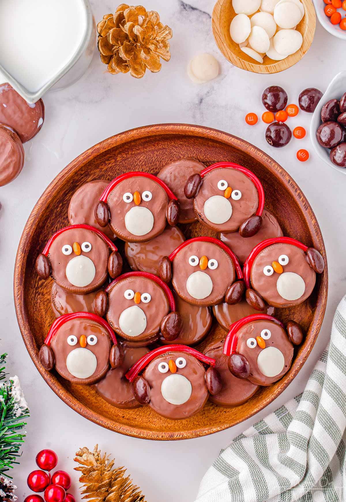 Top down shot of oreo penguins in a large round wood tray. Each penguin is decorated with red candy earmuffs.