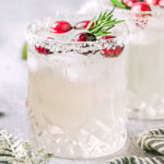 Christmas margarita in a short glass topped with fresh cranberries and a sprig of rosemary, Another glass can be seen in the background.