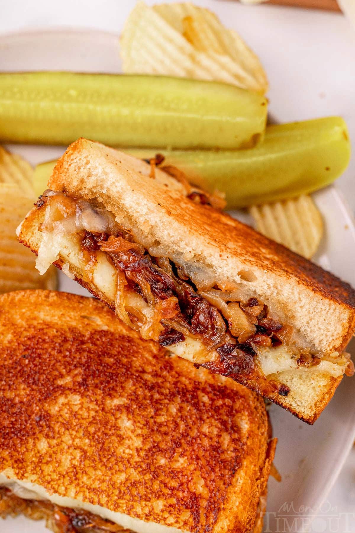 French Onion soup grilled cheese sandwich cut in half on a plate with pickle spears and chips.