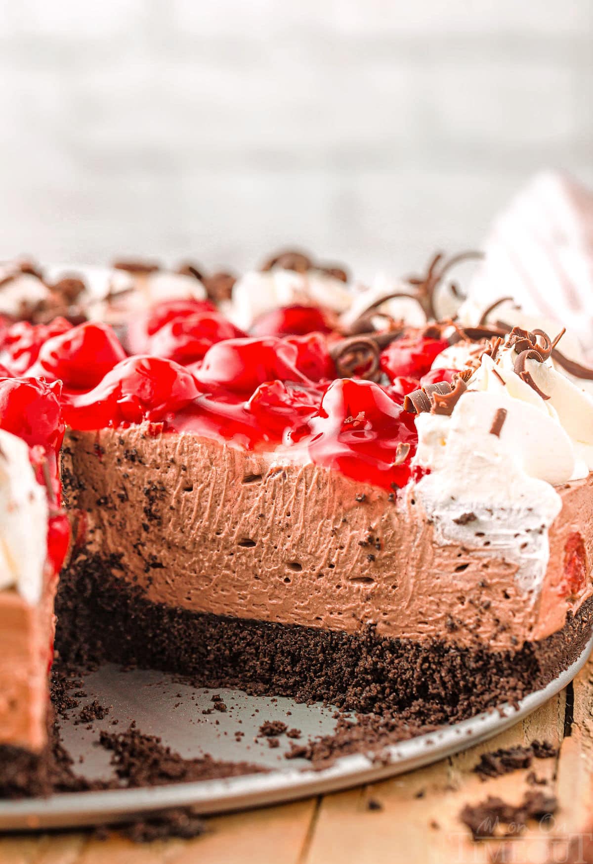 Cross section of black forest cheesecake showing creamy chocolate cheesecake and cherry pie filling topping along with whipped cream.